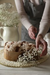 Obraz na płótnie Canvas Woman decorating delicious Italian Easter dove cake (traditional Colomba di Pasqua) with flowers at white wooden table, closeup