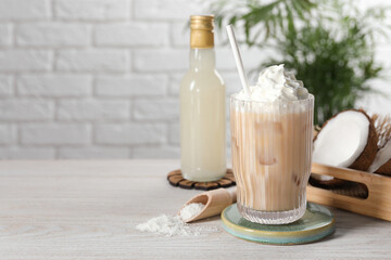 Bottle of delicious syrup, glass of iced coffee, coconut and flakes on white wooden table, space for text
