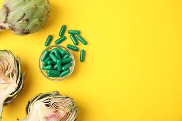 Bowl with pills and fresh artichokes on yellow background, flat lay. Space for text