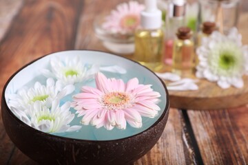 Bowl with water and beautiful flowers on wooden table, closeup. Spa composition