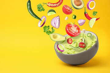 Delicious guacamole with flying ingredients on yellow background, space for text