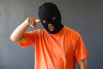 Prisoner in orange shirt and black mask pointing finger to camera over grey wall