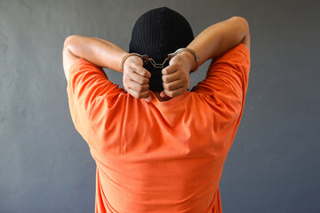 Rear view of a prisoner in orange t-shirt wearing handcuff isolated over grey background