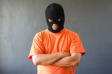 Portrait of a prisoner in orange shirt and black mask over grey wall