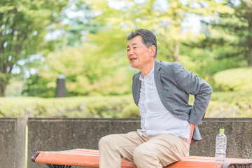 Fototapeta na wymiar 公園のベンチに座る高齢者の男性（腰痛） 