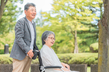 車椅子に乗って散歩する日本人の高齢者夫婦
