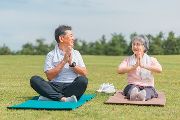 公園でヨガ・運動するアジア人の高齢者夫婦（合掌）
