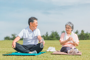 公園で運動して水分補給・水を飲むアジア人の高齢者夫婦（ヨガ）
