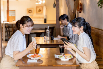 カフェでスマホを見ながら話す・おしゃべりする笑顔の若いアジア人女性たち
