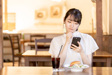 ランチを食べに来たカフェや飲食店の口コミ・SNSをスマホで見るアジア人女性
