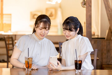 カフェでスマホを見ながら話す笑顔のアジア人女性

