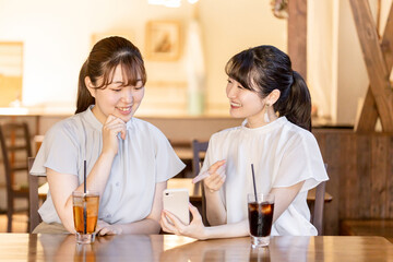 カフェでスマホを見ながら話す若いアジア人女性
