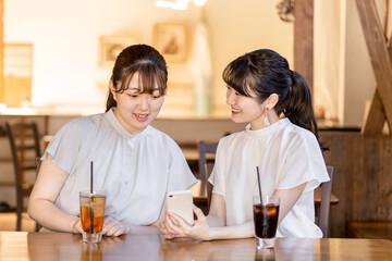 カフェでスマホを見ながら話す笑顔のアジア人女性
