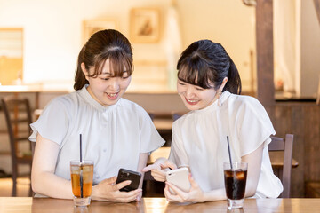 カフェや喫茶店でスマホを見ながら話す若いアジア人女性
