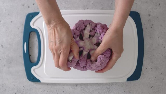 Woman devided purple cauliflower into florets, the cooking process, view from above. 