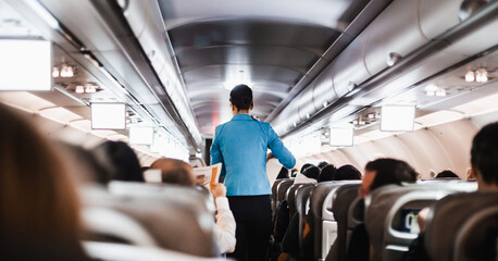 Interior of airplane with passengers on seats and stewardess in uniform walking the aisle, serving people. Commercial economy flight service concept