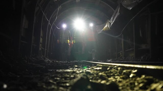 Workers with helmets and equipment walking in chrome mine tunnel