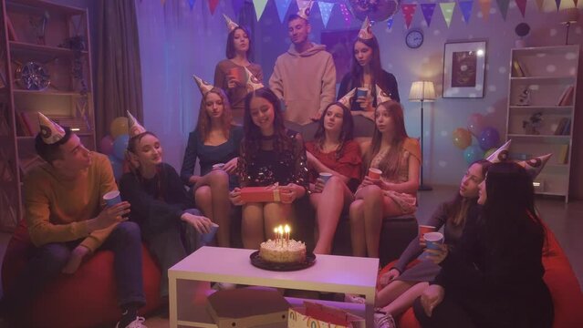 Time to make a wish. The birthday girl makes a wish and blows out the burning candles on the cake. Friends congratulate her on her birthday and clap their hands. Party. HDR BT2020 HLG Material.