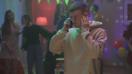 A guy at a home party is emotionally talking on the phone while his friends are dancing. He proves something, argues and, upset, hangs up. Video 2 in 1. HDR BT2020 HLG Material.