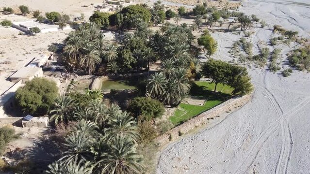 Aerial View Of Village Located In Khuzdar With Lush Green Trees And Gardens Surrounded By Desert Landscape. Parallax Shot