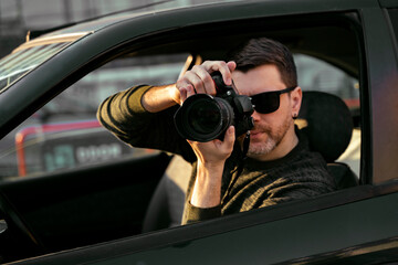 Man detective or agent taking photos from the car, wearing modern sunglasses 