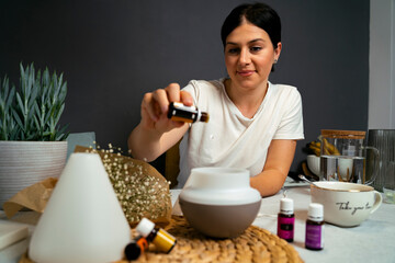 Young woman putting essential oils into diffuser, air quality at home concept 