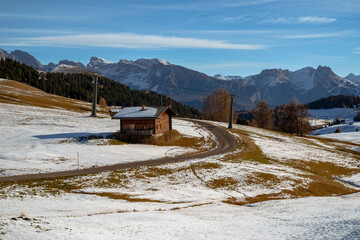 A cottage with cable car pylons behind a tall, snow-capped mountain in the Dolomites, Italy.
