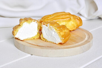Delicious pastries. A broken cake with an airy white cream on a wooden board on a white background