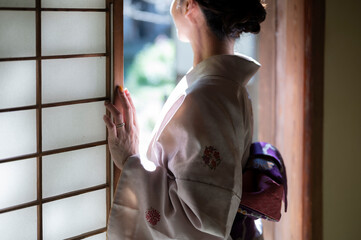 着物姿の女性が和室の窓から庭を眺めている