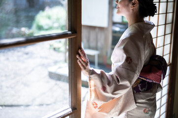 着物姿の女性が和室の窓から庭を眺めている