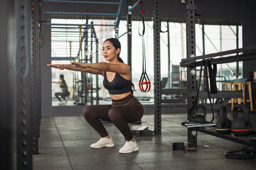Strong Asian woman doing squat exercise at cross fit gym. Athlete female wearing sportswear workout on grey gym background with weight and dumbbell equipment. Healthy lifestyle.