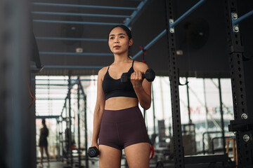 Fototapeta na wymiar Strong Asian woman doing exercise with dumbbell at cross-fit gym. Athlete female wearing sportswear workout on grey gym background with weight and dumbbell equipment. Healthy lifestyle.