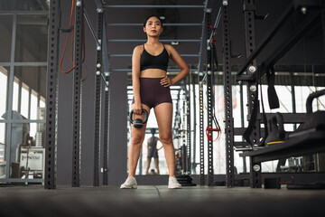 Obraz na płótnie Canvas Strong Asian woman doing exercise with kettlebell at cross fit gym. Athlete female wearing sportswear workout on grey gym background with weight and dumbbell equipment. Healthy lifestyle.