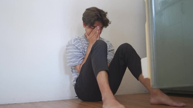 Depressed young Asian sad man sitting on the floor in the kitchen and crying. Loneliness guy living alone with negative thoughtful feeling break up and stressed. Mental health and life problem concept