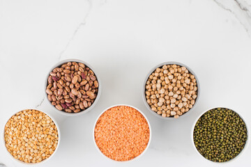 Legumes in glass jars top view on white background. Vegetable protein, healthy eating. Copy space