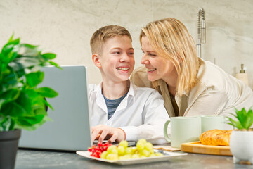 Happy mother and son have healthy breakfast in the kitchen at home. Happy mother and son in the kitchen. breakfast and digital devices Concept of happy family and healthy food.