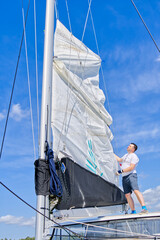 Raising the sail on a yacht. Young man captan lifting the sail of catamaran yacht during cruising....