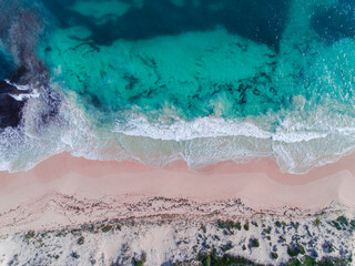Fototapeta na wymiar Aerial view of pink sandy beach with waves. Sunny day in summer with transparent tropical blue water. Summer seascape beautiful waves, blue sea water on a sunny day. Top view from drone. Sea aerial