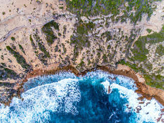 Aerial top down view of cliffs and clear blue water. Ocean waves smashing on the cliffs as a...
