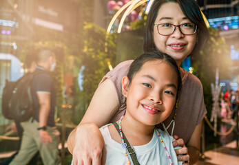 Portrait Asian middle-aged mother and little daughter in a shopping mall, focus on the child, blurred background of unidentified people in the mall.