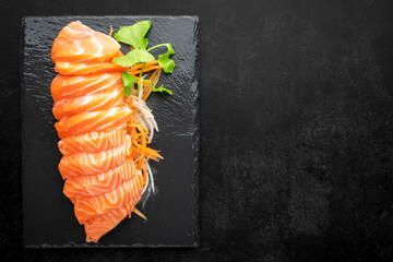 top view of fresh salmon sashimi fillet with carrot, radish slice and celery in black slate on dark tone texture background with copy space for text