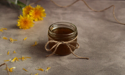 Dandelion flower jam in a glass jar on a gray background