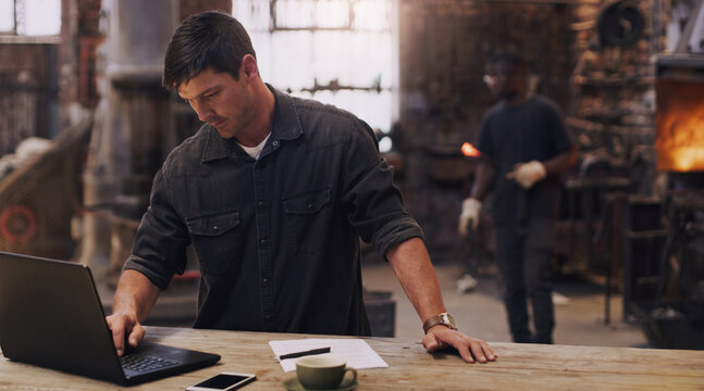 Workshop, man and working on laptop in metal blacksmith factory for trade business, finance and industry technology. Welder, computer and online paperwork for businessman, staff and forge worker - Powered by Adobe