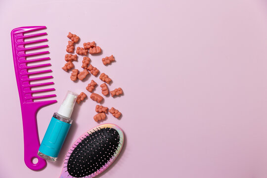 Hair care items and hair vitamin gummies on a pink background