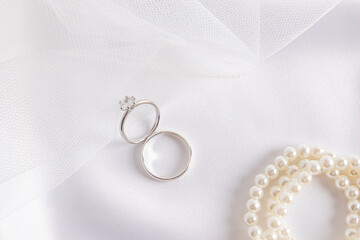 Two white gold rings with a diamond on the part of the bride's wedding veil and satin white textiles with pearl beads. Wedding composition.