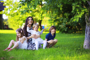 Fototapeta premium Young large family on a summer morning walk. Beautiful mother with children is playing in the park.