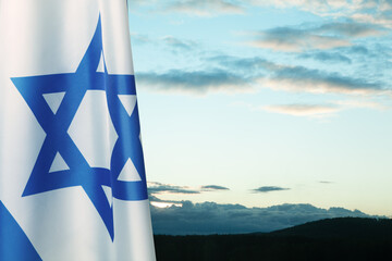 Israel flag with a star of David over cloudy sky background on sunset. Banner with place for text.