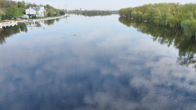 Trees and blue sky with clouds reflected in the smooth surface of the dark river. View from above. A beautiful landscape. White clouds reflecting on the surface of the water