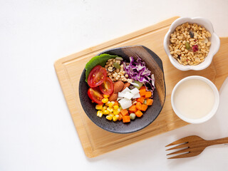 Mixed vegetable salad with tomato, corn, carrot, green peas, red cabbage, cos lettuce, granola, crispy coconut chips on borwn bowl over cutting board. Healthy food and weight loss concept. .