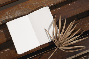 Open blank notebook on the wooden table with dried palm branch. Summer modern mock up, copy space for your text.
